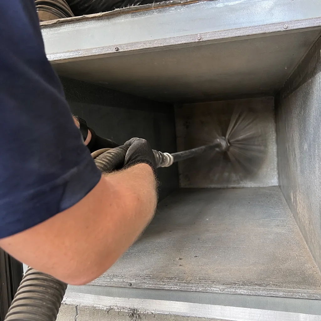 Technician using a rotating brush to clean inside metal air ducts